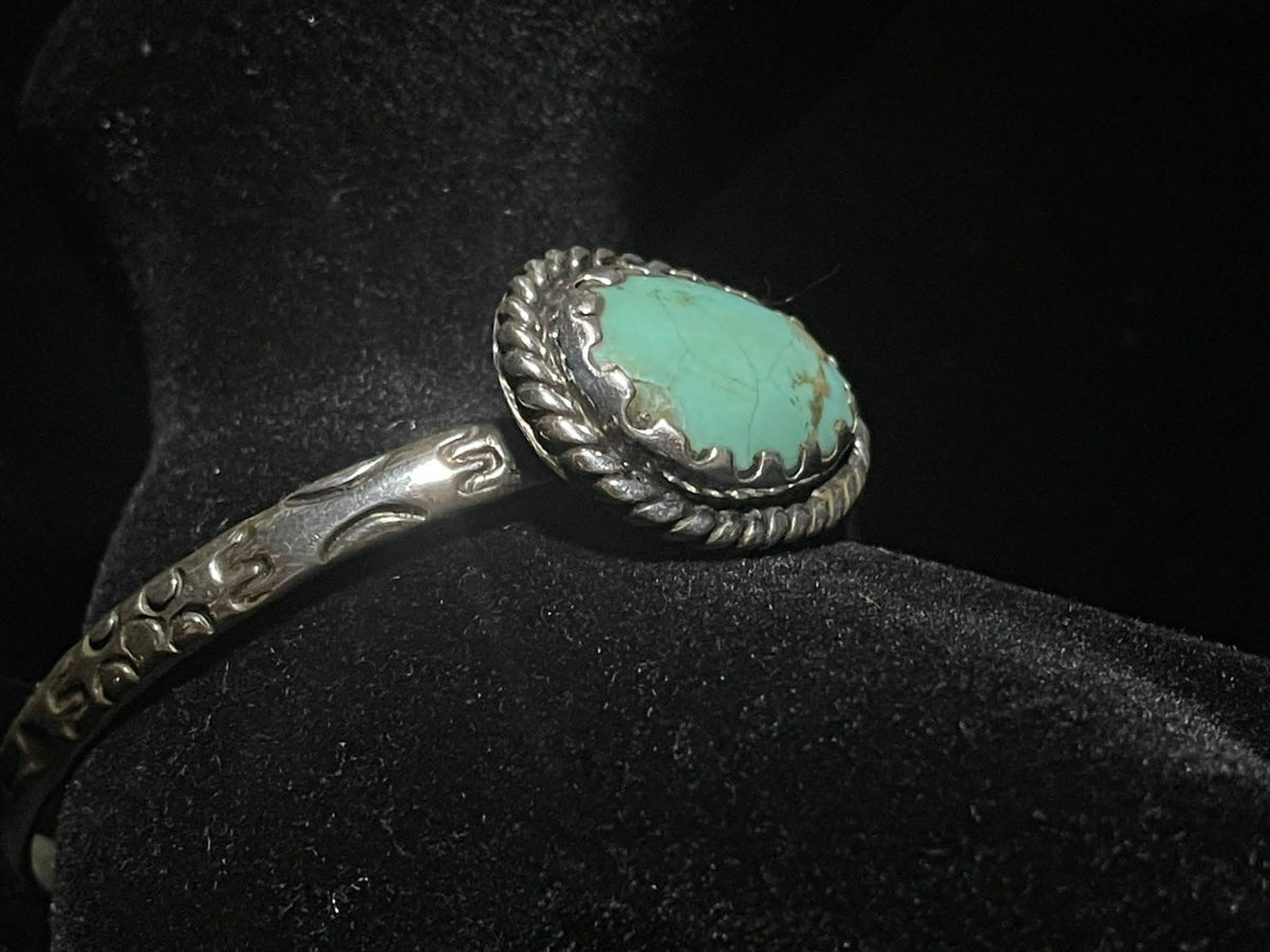 Turquoise cuff bracelet — oval turquoise stone in a rope bezel with the stamped sterling band, side view on black