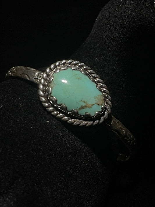 Turquoise cuff bracelet — one oval pale green-blue Sonoran turquoise stone in a rope bezel, front view on black