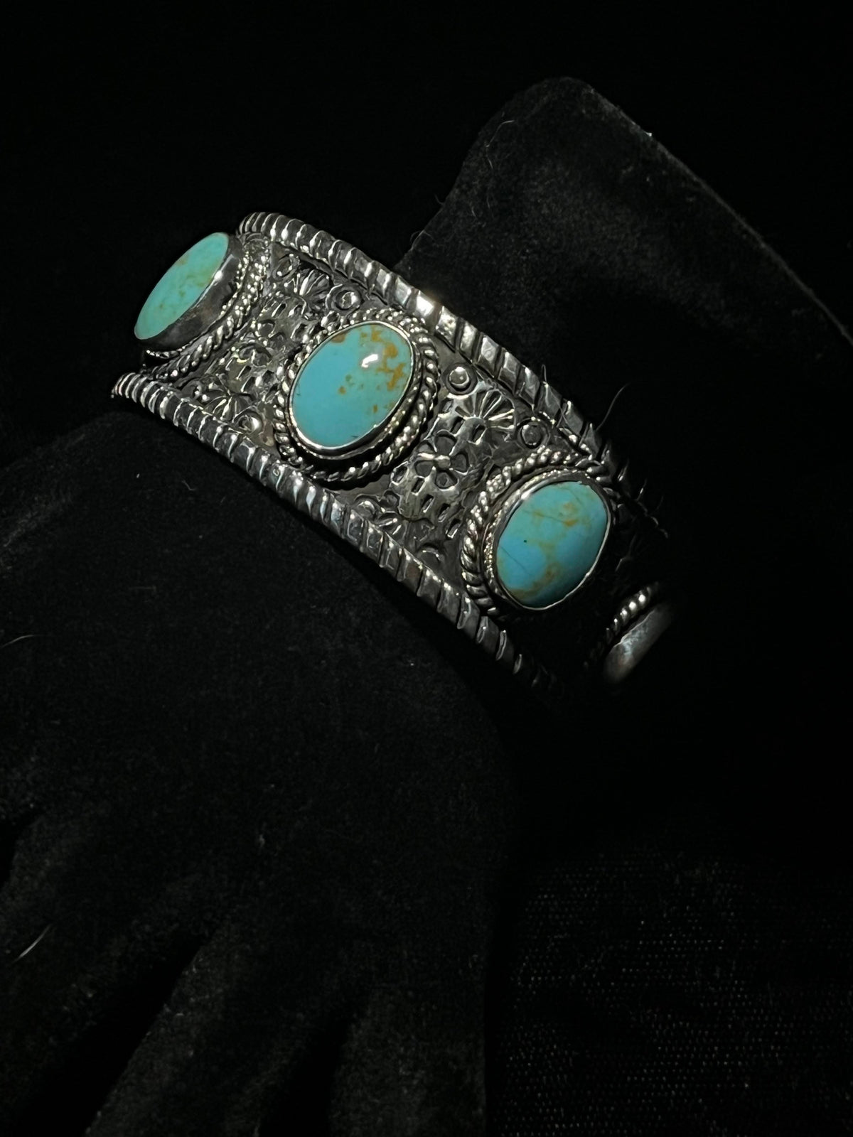 Turquoise cuff — three oval turquoise stones in rope bezels on a stamped silver band, angled close view